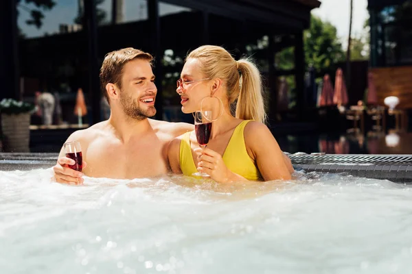 Sexy couple holding glasses of red wine in swimming pool in sunny day — Stock Photo