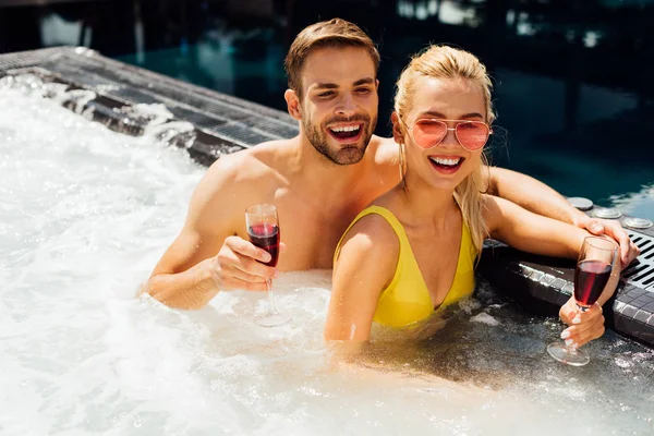 Coppia sexy che tiene bicchieri di vino rosso che abbraccia in piscina nella giornata di sole — Foto stock