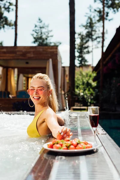 Menina sexy em maiô com vinho tinto e morangos na piscina — Fotografia de Stock