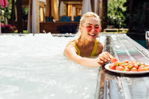 Menina sorridente sexy em maiô com morangos na piscina — Fotografia de Stock