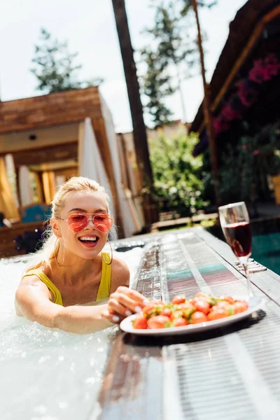 Chica sexy en traje de baño con vino tinto y fresas en la piscina - foto de stock