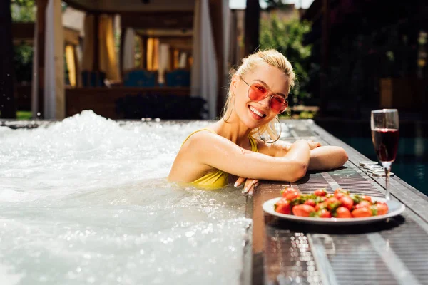 Sexy ragazza in costume da bagno con vino rosso e fragole in piscina — Foto stock