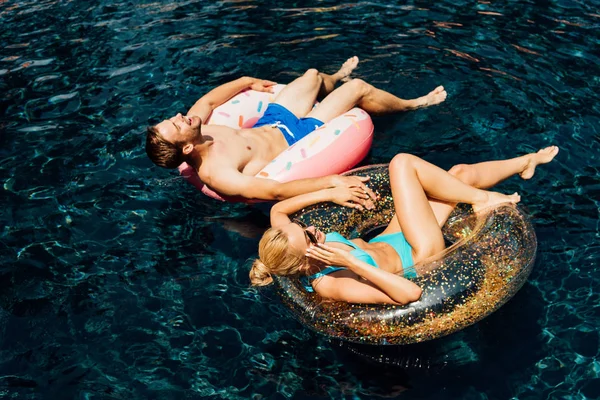 Glückliches Barfußpaar liegt auf Schwimmringen im Schwimmbad — Stockfoto