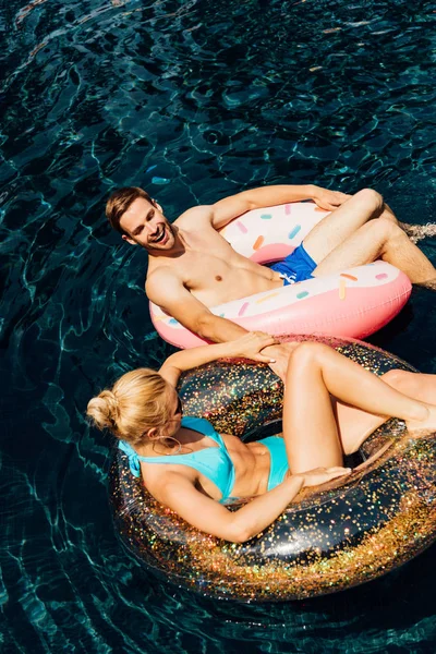 Happy barefoot couple lying on swim rings in swimming pool — Stock Photo
