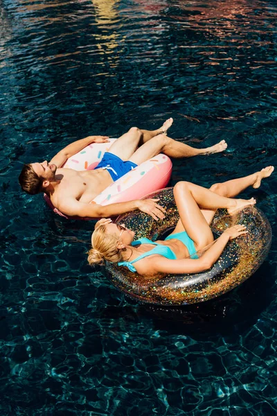 Feliz pareja descalza tumbada en los anillos de natación en la piscina - foto de stock