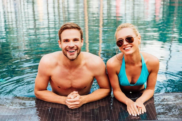 Sonriente feliz pareja en piscina mirando a la cámara - foto de stock