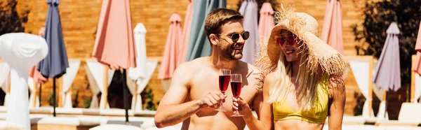 Panoramic shot of sexy couple holding wine glasses with red wine at resort — Stock Photo