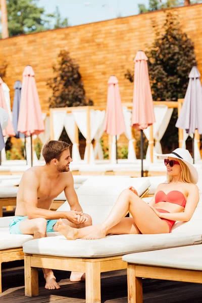 Sexy sorrindo casal olhando uns para os outros em espreguiçadeiras no resort em dia ensolarado — Fotografia de Stock
