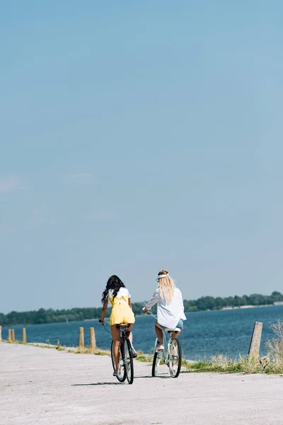 Вид ззаду блондинка і брюнетка друзі катаються на велосипедах біля річки влітку — стокове фото