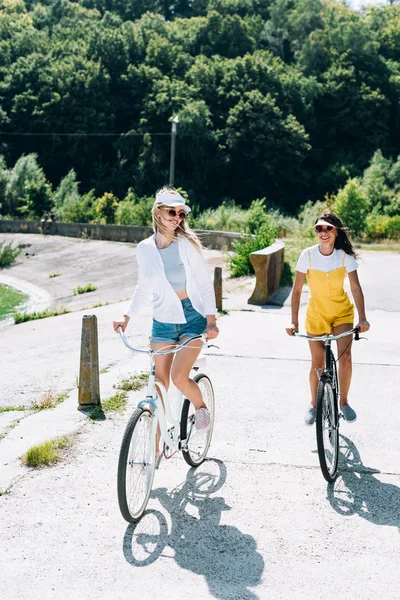 Chicas rubias y morenas felices montando bicicletas en verano - foto de stock