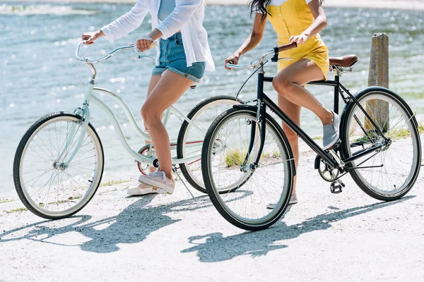 Cropped view of girls riding bikes near river in summer — Stock Photo