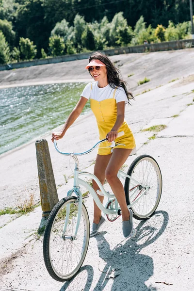Brunette beautiful girl riding bicycle near river in summer — Stock Photo