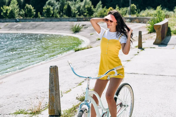 Улыбающаяся брюнетка красивая девушка катается на велосипеде у реки летом — стоковое фото
