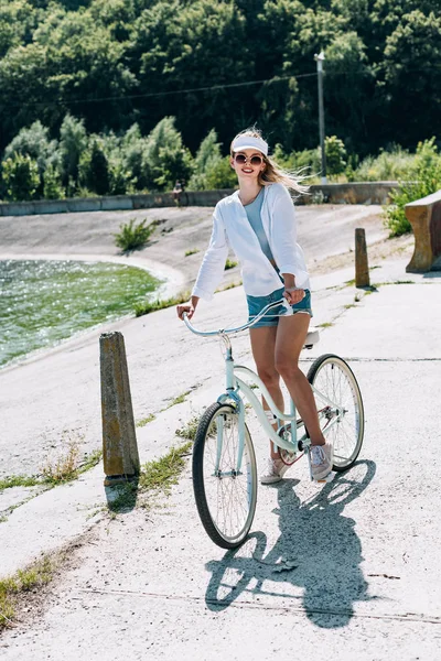 Блондинка їде на велосипеді біля річки влітку — стокове фото