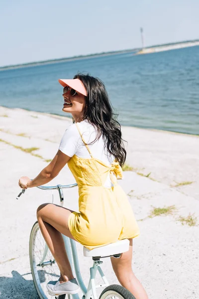 Chica morena feliz montar bicicleta cerca del río en verano - foto de stock