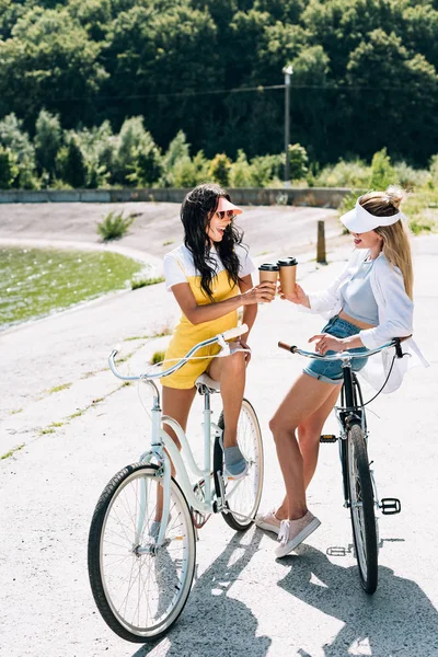 Meninas loiras e morenas felizes com bicicletas e café para ir perto do rio no verão — Fotografia de Stock