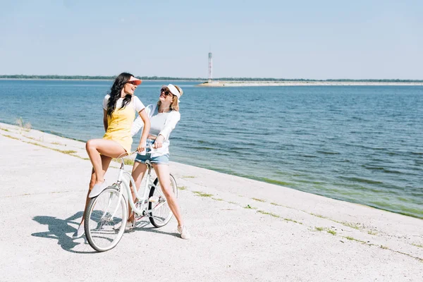 Chicas rubias y morenas con bicicleta cerca del río en verano - foto de stock