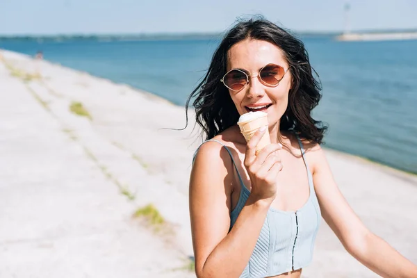 Happy brunette girl eating ice cream and riding bike near river in summer — Stock Photo