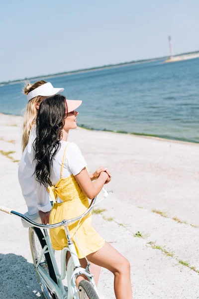 Vista lateral de meninas com bicicleta olhando para o rio no verão — Fotografia de Stock