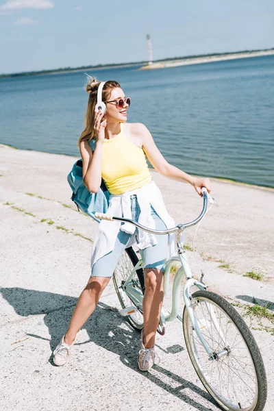 Blondes Mädchen radelt im Sommer in Flussnähe und hört Musik über Kopfhörer — Stockfoto