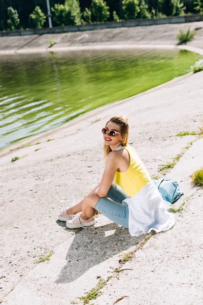 Glückliches blondes Mädchen, das im Sommer am Fluss sitzt — Stockfoto