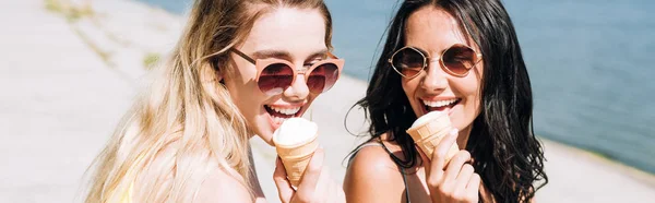 Plano panorámico de chicas rubias y morenas felices comiendo helado - foto de stock