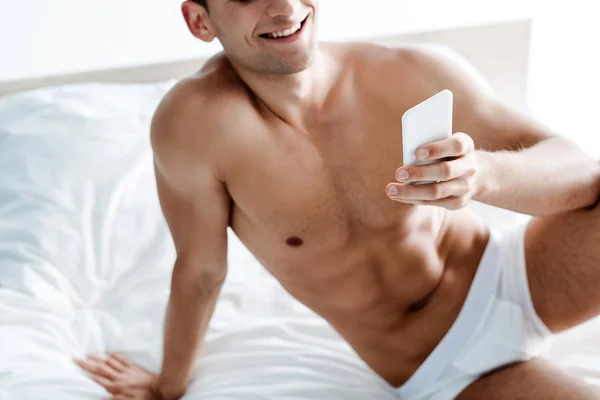 Ausgeschnittene Ansicht eines fröhlichen, hemdslosen Mannes mit Smartphone im Schlafzimmer — Stockfoto