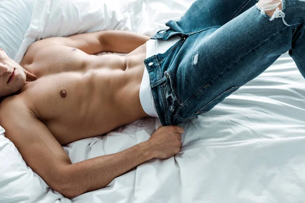 Обрезанный вид сексуального мужчины снимающего синие джинсы, лежащего на кровати — стоковое фото