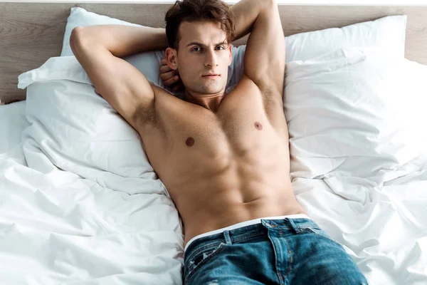 Сексуальный мужчина в джинсах в джинсах лежит на кровати дома — стоковое фото