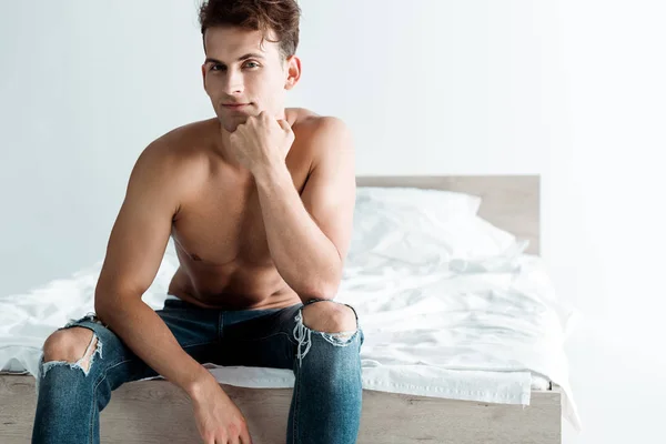 Sexy giovane uomo in jeans blu seduto sul letto a casa — Foto stock