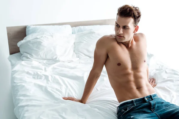 Homme sexy en jeans denim assis sur le lit à la maison — Photo de stock
