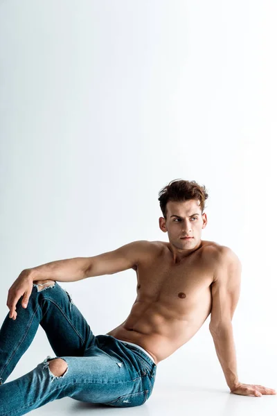 Sexy jovem homem no azul jeans jeans sentado no branco — Fotografia de Stock