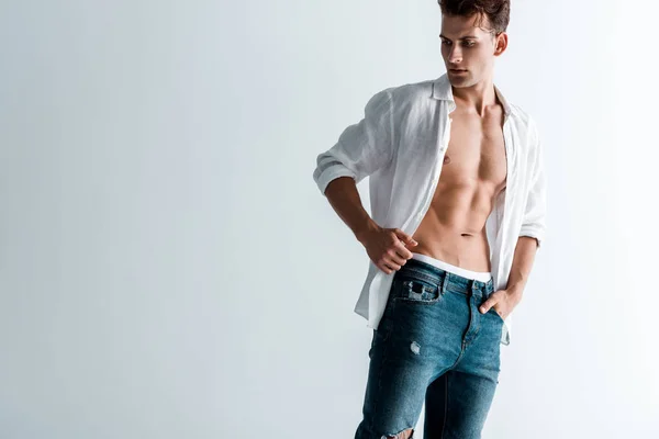 Sexy man in jeans and shirt standing with hand in pocket on white — Stock Photo