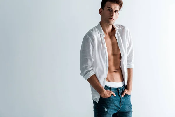 Bel homme en jeans et chemise debout avec les mains dans les poches sur blanc — Photo de stock