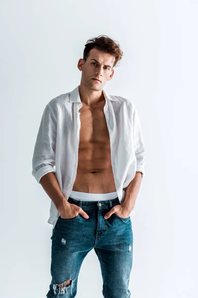 Hombre guapo en jeans y camisa de pie con las manos en bolsillos aislados en blanco - foto de stock