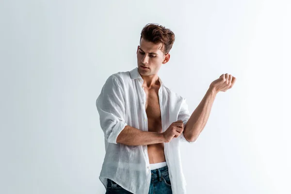 Красивый молодой человек трогает рубашку, стоя на белом — стоковое фото