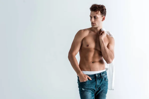 Muscoloso giovane uomo in jeans denim in piedi con mano in tasca e tenuta camicia isolata su bianco — Foto stock