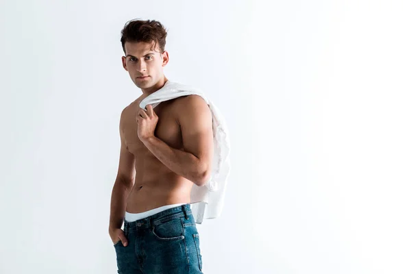 Sexy homem no azul jeans segurando camisa e de pé com a mão no bolso isolado no branco — Fotografia de Stock