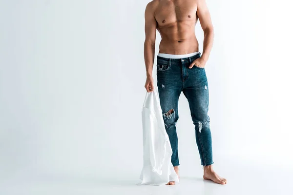 Cropped view of sexy man holding shirt and standing with hand in pocket on white — Stock Photo