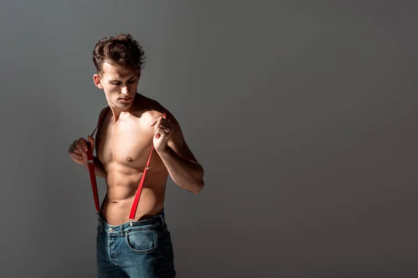 Hemdloser und gutaussehender Mann, der auf roten Hosenträgern steht und isoliert auf grau schaut — Stockfoto