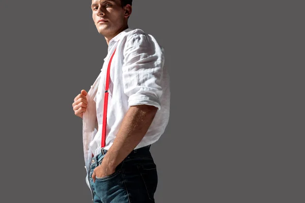 Красивий чоловік торкається білої сорочки, стоячи з рукою в кишені ізольовано на сірому — стокове фото