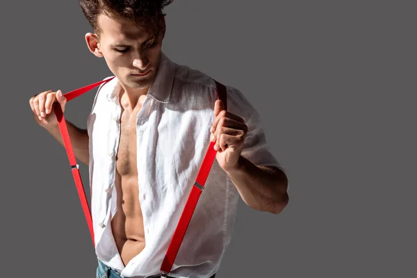 Hombre guapo en camisa blanca tocando tirantes rojos aislados en gris - foto de stock