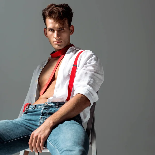 Sexy Mann im weißen Hemd sitzt isoliert auf grau — Stockfoto