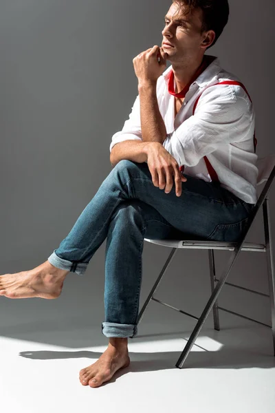 Nachdenklicher Mann im weißen Hemd sitzt auf Stuhl auf grau — Stockfoto