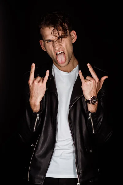 Жестокий человек, торчащий языком и показывающий рок-знак, изолированный на черном — стоковое фото