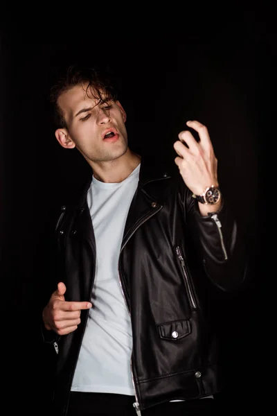 Stylish young man in leather jacket gesturing isolated on black — Stock Photo