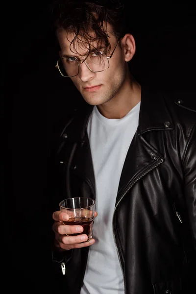 Homem na moda em óculos de olho segurando vidro com uísque isolado em preto — Fotografia de Stock