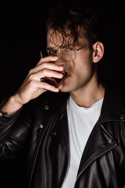 Hombre de moda sosteniendo vidrio y beber whisky aislado en negro - foto de stock