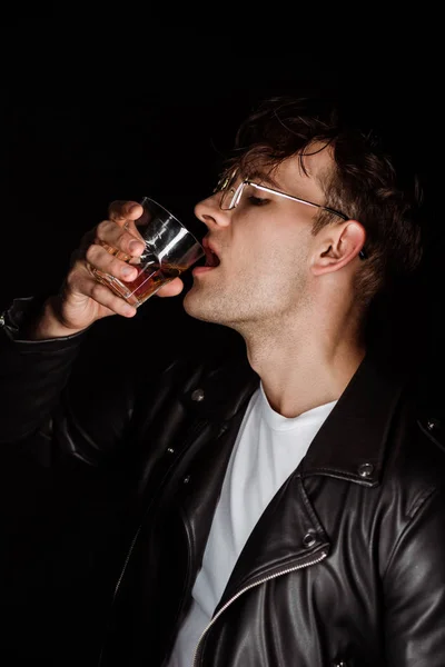 Brutal hombre sosteniendo vidrio y bebiendo whisky aislado en negro - foto de stock