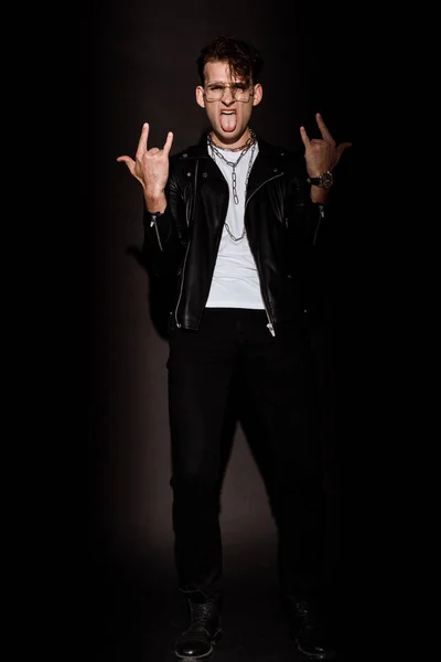 Trendy man in glasses showing rock sign while sticking out tongue on black — Stock Photo